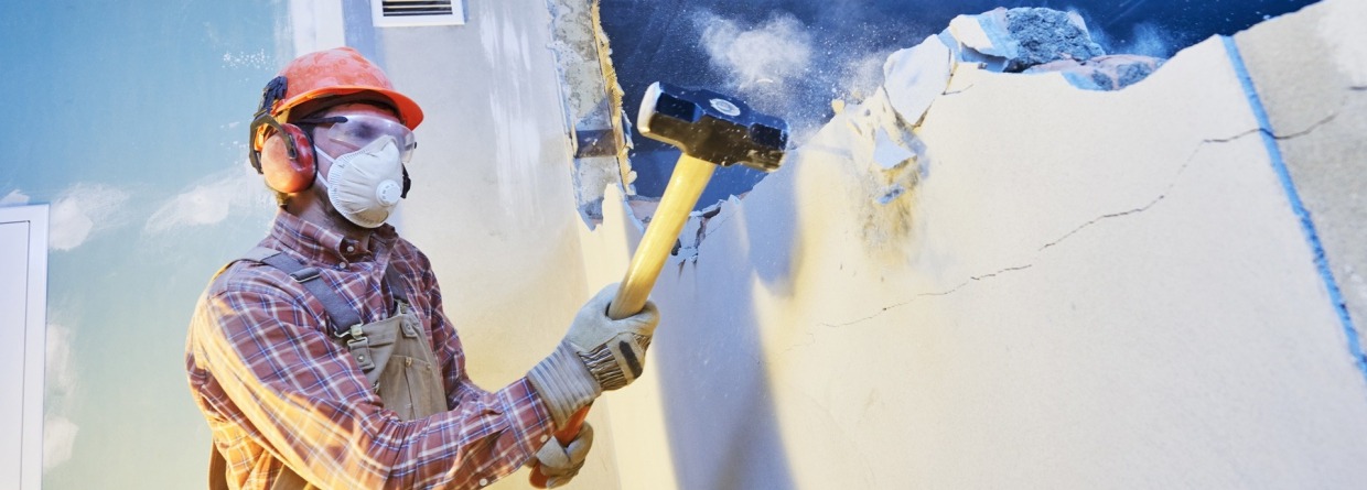 Man slaat met een hamer de binnenmuur van een huis kapot